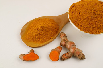 Turmeric powder in a wooden spoon and turmeric roots separately on a white background, used as a tonic for the body and food ingredients.