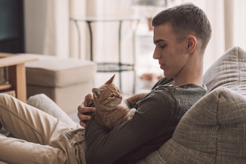 Handsome teenage guy relaxing on modern soft couch at home in living room