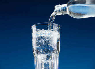 Drinking water pours from a bottle into a glass with ice