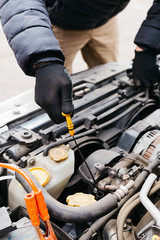 Man in black gloves checking the oil level in a car outdoors in winter. Car mechanic engineer working in car repair service. Male hands fixing a car, checking the oil level.