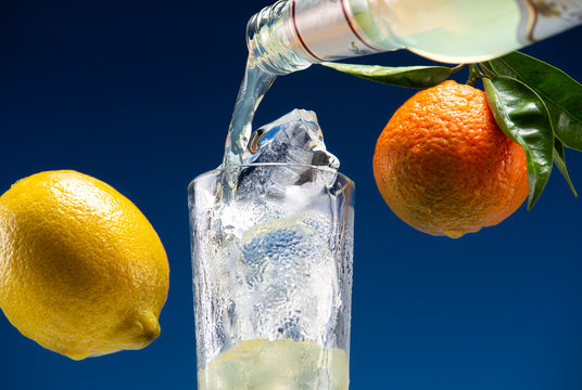 Carbonated drink pours from a glass bottle into a glass with ice