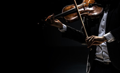 The violinist in a tailcoat plays the violin on a dark background.