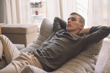 Handsome teenage guy relaxing on modern soft couch at home in living room