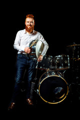 Fototapeta na wymiar Attractive bearded man drummer sitting and playing on his kit over dark background. Stylish man with drums and drum kit