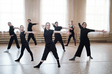 Horizontal shot of professional young dancers wearing black outfits rehearsing their new dance in studio