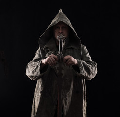 monk in a hood with a sword on a black background