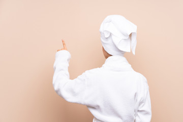 Teenager girl in a bathrobe over isolated background pointing back with the index finger