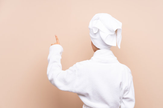 Teenager girl in a bathrobe over isolated background pointing back with the index finger