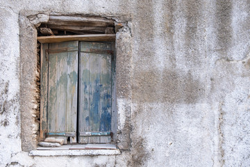 Old double closed wooden shutters. Rusty hinges on peeled planks,  stones keep the window shut. Wall blank and faded. Copy space.