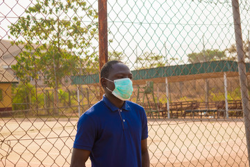 young black man standing alone outside wearing a medical face mask