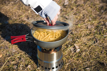 close up of hiker's hands cooking pasta on portable wood stove. Cooking pasta in mountains
