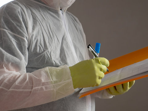 elderly man in protective overalls with orange folder and pen, special glasses and bactericidal mask. military pensioner ready to fight with coronovirus and treat the room with special solution
