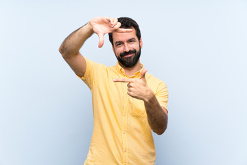 Naklejka premium Young man with beard over isolated blue background focusing face. Framing symbol