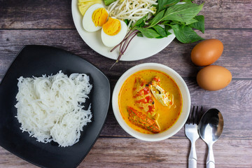 Thai rice noodles in grab curry sauce with vegetable and boiled eggs on wood table. Thai food style...