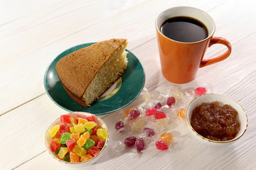 A cup of coffee with cake, candy, candied fruits and jam on a wooden table.