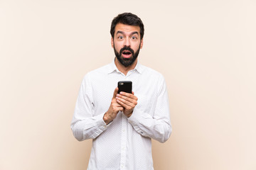 Young man with beard holding a mobile surprised and sending a message