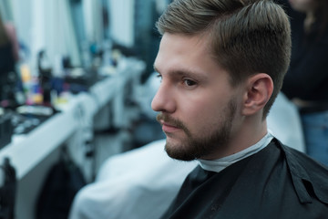 close up portrait of a young bearded guy sitting at the hairdresser while barbershop