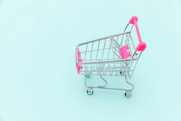 Small supermarket grocery push cart for shopping toy with wheels isolated on blue pastel colorful trendy background Copy space. Sale buy mall market shop consumer concept.