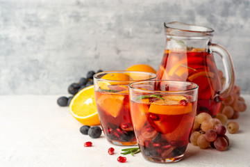Homemade sangria with orange, grapes and pomegranate seeds in glasses on concrete background. Selective focus.