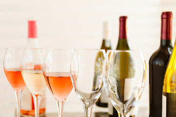 Wine tasting set in the light airy environment. Custom wine tasting concept. Glasses of wine and bottles on the glass table and light background.