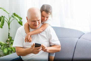 Little girl with her grandfather using smartphone at home, space for text. Family time