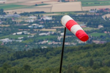 Fototapeta na wymiar Red and white windsock measuring stormy windy weather at hill. Meteorology measurement instrument show wind force at hurricane. Forecast of dangerous storm intensity for cyclone or high in nature
