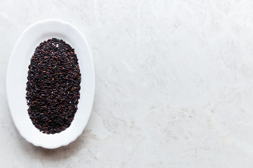 Black wild rice in a white plate close-up on a white background, selective focus