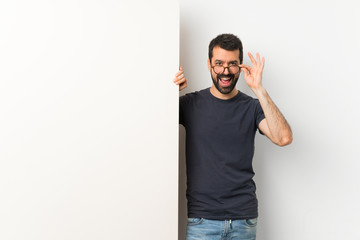 Young handsome man with beard holding a big empty placard with glasses and smiling