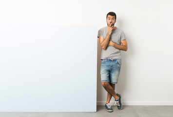 Young handsome man with beard holding a big blue empty placard surprised and shocked while looking right © luismolinero