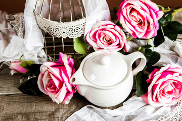 White cage and a tea pot with roses and decoration on a wooden table