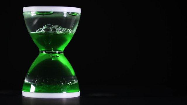 hourglass with green liquid dripping on a black background, leaking time concept with free space 