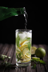 Cool Mojito with mint and lime. Water is poured from a bottle in the summer heat on a dark background. Background image, copy space