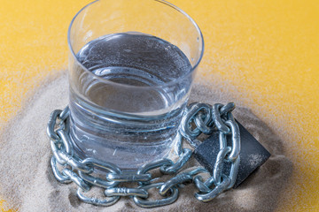 a glass of water entwined in a chain and closed with a padlock, standing on the sand.  Global warming, decreasing world drinking water resources