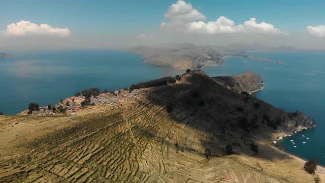Aerial view of the Island of the Sun (Isla del Sol) in Lake Titicaca in the Andes Mountains at the border between Bolivia and Peru. Hilly dry landscape with small village surrounded by deep blue water