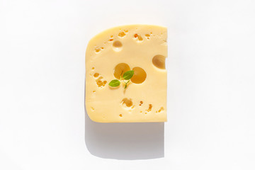 Creative cheese with hard sunlight shadows white background flat lay. Healthy breakfast sandwich concept, calcium rich dairy food,top view,copy space. Yellow delicious snack with holes and green leaf.