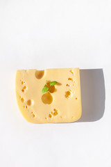 Creative cheese with sunlight shadow on a white background flat lay. Healthy breakfast sandwich concept, calcium rich dairy food, top view,copy space. Yellow delicious snack with holes and green leaf.