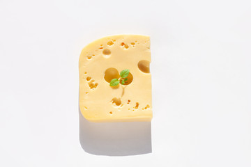 Creative cheese with hard sunlight shadows white background flat lay. Healthy breakfast sandwich concept, calcium rich dairy food,top view,copy space. Yellow delicious snack with holes and green leaf.