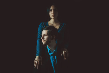 Art portrait of a guy who holds in a rue a glass of wine, with the girl next to him, on a dark background. Dramatic light. Author's creative tinting