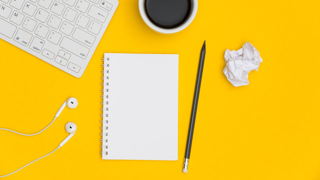 Blank spiral notepad with keyboard, supplies and pencil on bright yellow background. Top view office desk with notepad. Creative flat lay photo