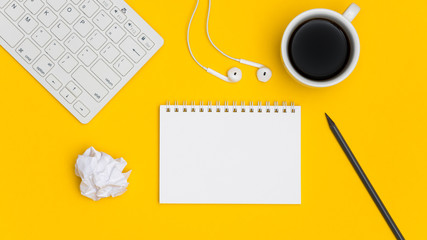 Blank spiral notepad with keyboard, supplies and pencil on bright yellow background. Top view office desk with notepad. Creative flat lay photo