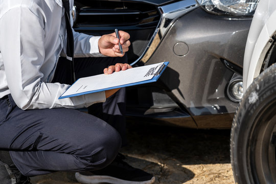 Insurance Agent Inspecting assessed Damaged Car checking and signing on report insurance claim form process after accident collision