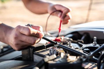 Mechanic repairman checking engine automotive in auto repair service and using digital multimeter testing battery to measure various values and analyze