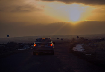 Fototapeta na wymiar Road traffic in the sunset. Car on asphalt under a cloudy sky.
