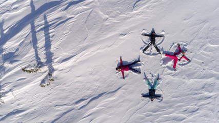 a group of young people in bright ski suits depict snow angels lying on the fresh snow in the form of a cross. four winter angels happy and energetic. Winter fun at the ski resort