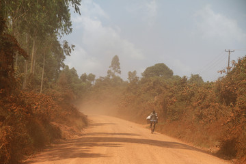 człowiek jadący na skuterze drogą szutrową na afrykańskiej prowincji © KOLA  STUDIO