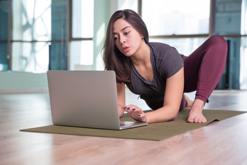 Photo of young woman practicing yoga with laptop indoor. Beautiful girl practice yoga in class. Yoga studio instructor. Blurred background.