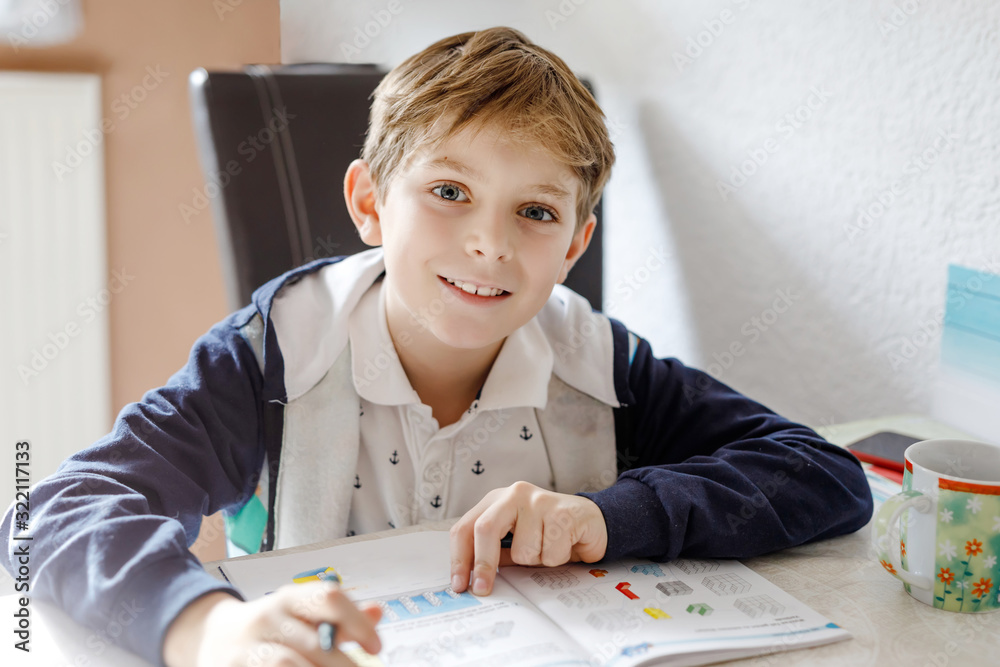 Wall mural portrait of cute happy school kid boy at home making homework. little child writing with colorful pe