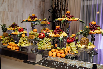 Different fresh fruits on wedding buffet table. Buffet for birthday party or wedding.  Decorated delicious. Buffet, assorted fresh fruits, berries and citrus. Preparation for design creative menu