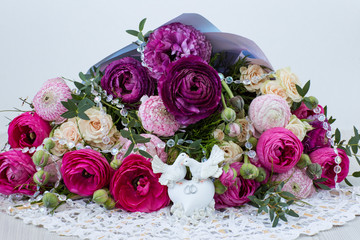 on a light background a bouquet of ranunculuses and roses are two white doves with wedding rings