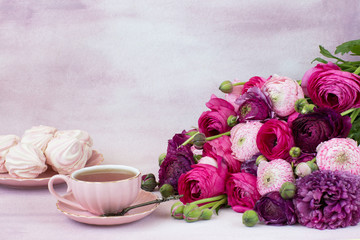 on a pink background a bouquet of ranunculus, a cup of tea and marshmallows in a plate
